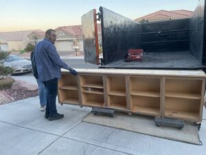 Two Tidy Toss Las Vegas, NV team members moving a long wooden cabinet on dollies for removal.