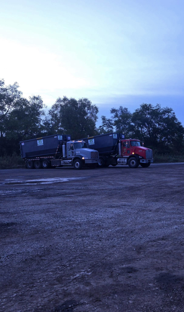 Two roll-off trucks with dumpsters parked in a lot, showcasing the fleet of Premier Recycling and Disposal in Waukesha, WI.