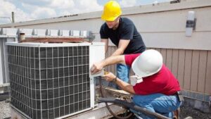 Two technicians in hard hats working on a large commercial rooftop air conditioning unit for Advanced Mechanical Contractors, Inc. in Nashville, TN.