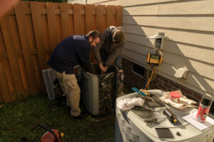 Two technicians from Cool Change Heating & Air servicing an outdoor air conditioning unit in Raleigh, NC.