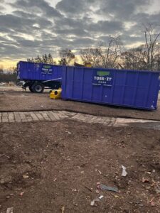 Two blue Toss-It roll-off dumpsters placed on a dirt construction site for debris removal in Baltimore, MD.