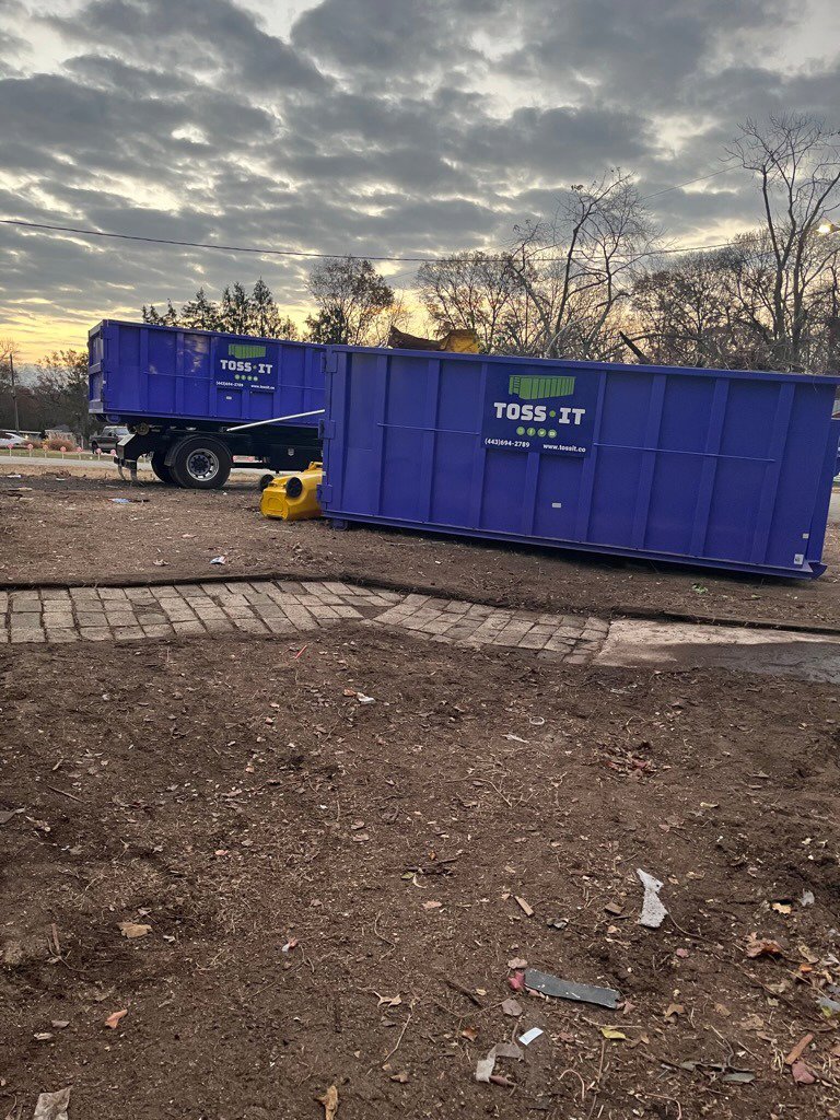 Two blue Toss-It roll-off dumpsters placed on a dirt construction site for debris removal in Baltimore, MD.