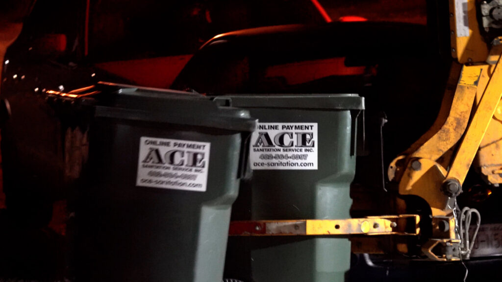Two Ace Sanitation Service Inc. trash bins being collected by a garbage truck at night in Columbus, NE.