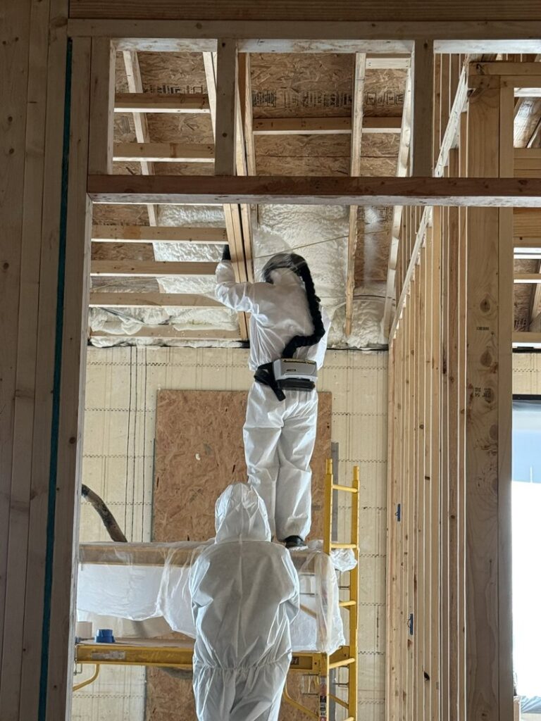 Two workers in protective suits applying spray foam insulation to walls and ceiling for Off-Axis Spray Foam and Radon Services in Clarksville, TN.
