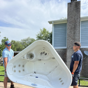 Two workers carrying a hot tub shell for removal by All That Junk Removal in Wilmington, NC.