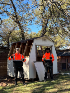 Two Grawe Junk & Demo workers in safety vests giving thumbs up in front of a partially demolished shed in Arlington, TX.
