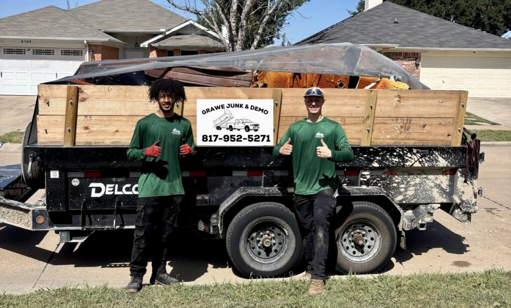 Two Grawe Junk & Demo workers stand in front of a dump trailer filled with various junk items, ready for removal in Arlington, TX.