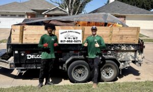 Two Grawe Junk & Demo workers stand in front of a dump trailer filled with various junk items, ready for removal in Arlington, TX.