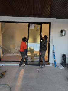 Two workers installing a large glass door panel during a home renovation project by JPS Home Builders LLC in Kenner, LA.