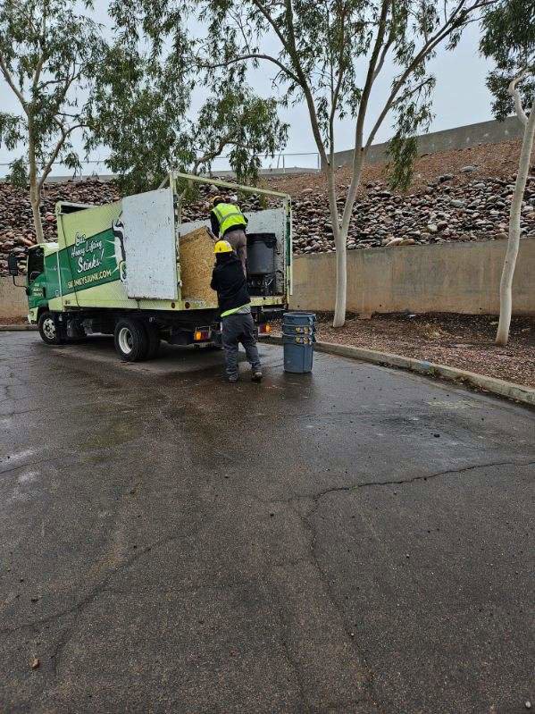 Two Skunky's Junk Removal workers loading a large bale and other items into their truck in Tempe, AZ.