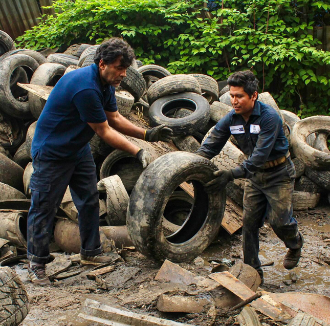 Two workers manually moving discarded tires from a large pile for Tire Waste Management in Newark, NJ.
