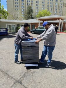 Two Goblins Junk Removal workers carefully moving a large, wrapped appliance or furniture item on a dolly in Wheat Ridge, CO.
