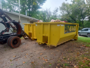 Two yellow roll-off dumpsters, one filled with debris, next to a truck for Tecumseh Rolloff Services in Moore, OK.