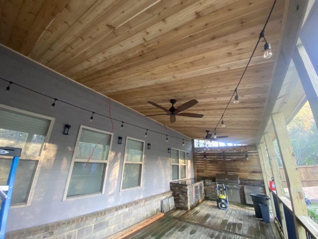 Underneath a newly built deck, showing a wooden ceiling, installed ceiling fans, and string lights by Stonehedge Construction in Buford, GA