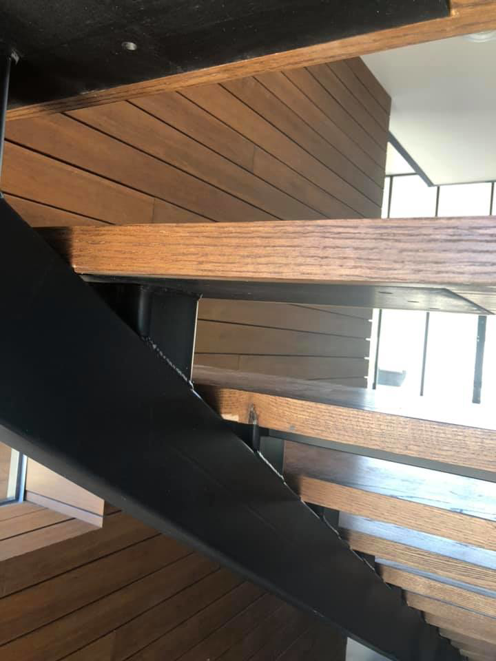 Underside view of a modern wooden staircase with metal support and wood paneling by Blackhawk Floors, Inc. in Scottsdale, AZ