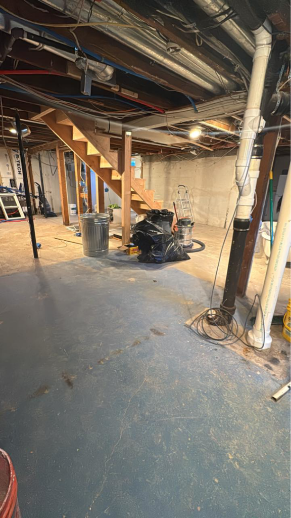 An unfinished basement showing renovation work in progress with exposed pipes and a wooden staircase by JP Handyman Wyo in Sheridan, WY