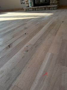 An unfinished hardwood floor with red installation markings near a stone fireplace by Cordell Hardwood Flooring in Lexington, KY.