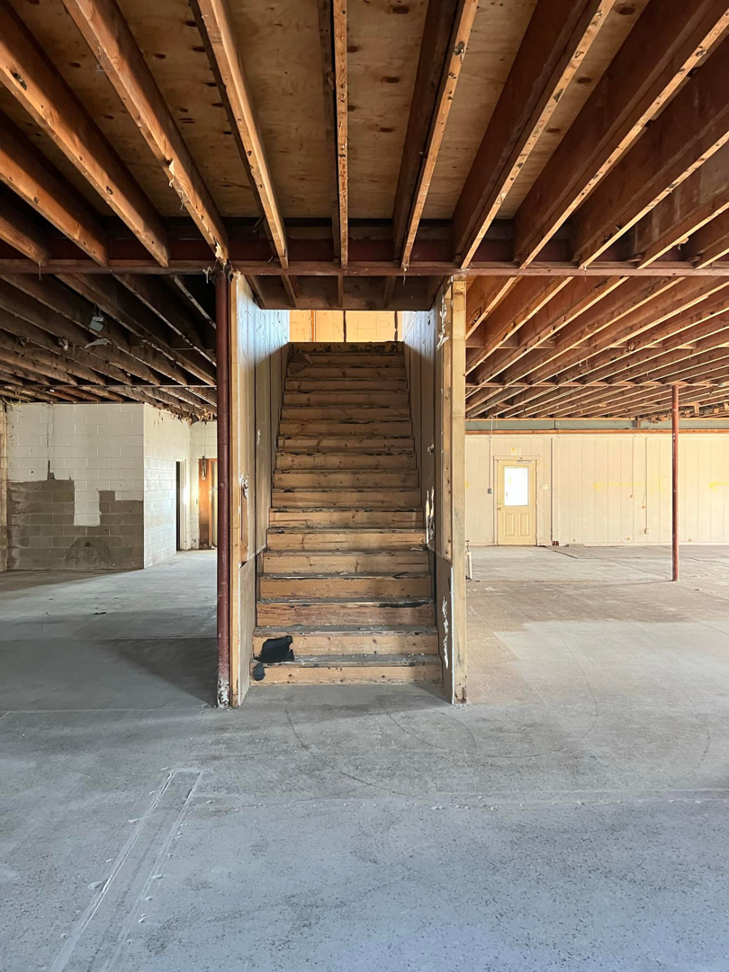 Unfinished interior space with exposed ceiling joists and wooden stairs during renovation by American Enterprises Inc. in Waunakee, WI.