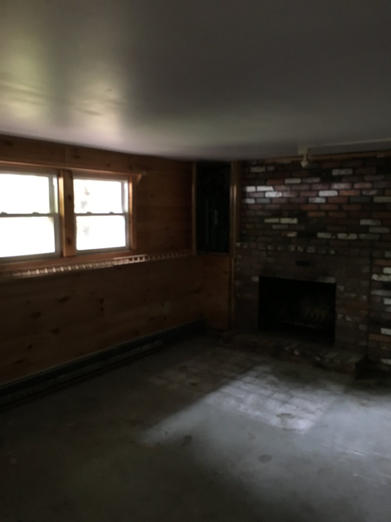 An unfinished room with wood paneling, a brick fireplace, and a concrete floor, ready for renovation by Lemelin General Contracting in Fall River, MA.