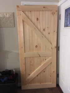 An unfinished custom wooden barn-style door ready for installation by Two Girls Cleaning Services in Brunswick, ME.