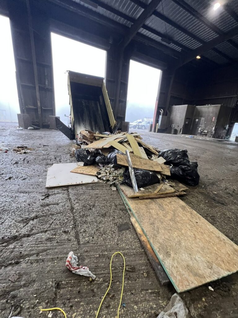 A dump trailer unloading black trash bags and wood debris at a transfer station, demonstrating service by Tidy Loaders Junk Removal in Houston, TX.