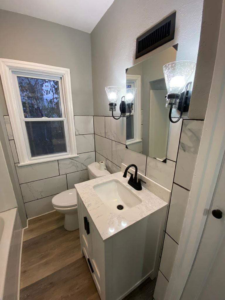 An updated bathroom featuring new wall tiles, a white vanity, mirror, and modern light fixtures by J&A Contractor LLC in Milwaukee, WI.