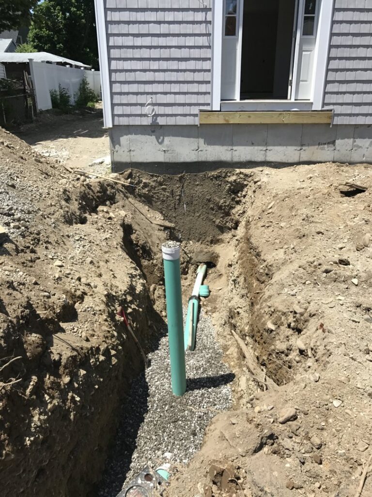 Utility pipes being installed in a trench next to a residential building by Solimini Excavation and Utility in Freetown, MA
