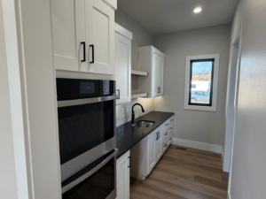 Utility room featuring white cabinetry, black countertop, and built-in ovens by ELS Construction in Springfield, MO.