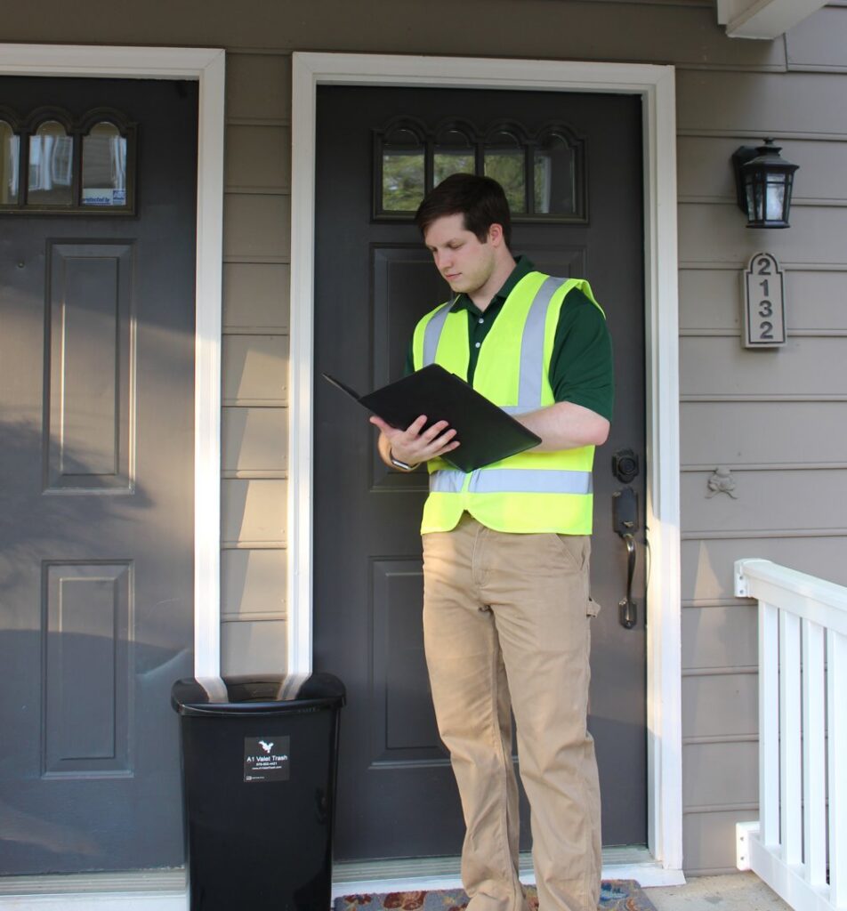 An A1 Valet Trash employee in a high-visibility vest standing next to a service bin in Atlanta, GA.