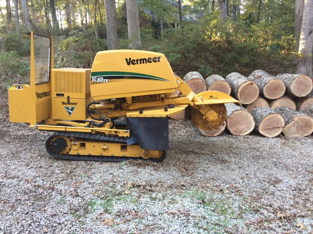 A Vermeer stump grinder parked next to a pile of freshly cut logs, showcasing equipment and results from Schnell Tree Services LLC in Fayetteville, NC.