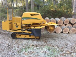 A Vermeer stump grinder parked next to a pile of freshly cut logs, showcasing equipment and results from Schnell Tree Services LLC in Fayetteville, NC.