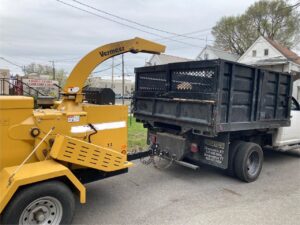Yellow Vermeer wood chipper connected to a dump truck, ready for debris removal after tree service by Sky High Tree Service in Lynnwood, WA.