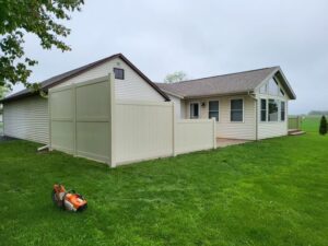 A light-colored vinyl fence recently installed around a house, with a power saw on the grass, by Badger Vinyl Products in Madison, WI.
