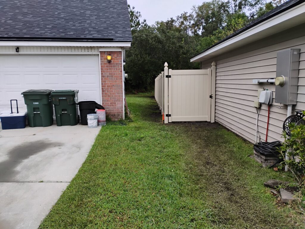 A newly installed light-colored vinyl privacy fence with a gate alongside a house by Fence & Deck Connection, Inc. in Savannah, GA.