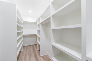 A spacious walk-in closet with custom white shelving and hanging rods installed by LP Home Builders in Houma, LA.