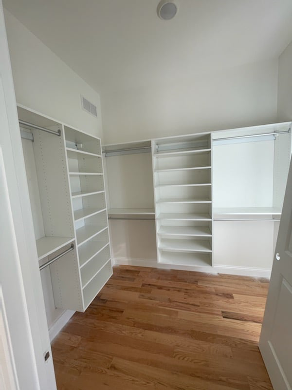Walk-in closet with white shelving and hanging rods installed by Thermal Concepts, Inc in St. Louis, MO.