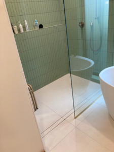 A modern walk-in shower featuring green subway tiles, a clear glass enclosure, and white floor tiles by Tess Tile By Design in Kansas City, MO.