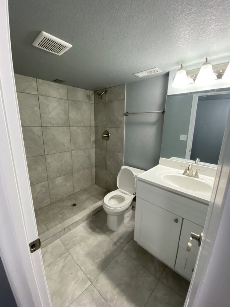 A newly installed walk-in tiled shower, toilet, and vanity in a remodeled bathroom by Advanced Remodeling Services in Elbert, CO.