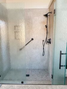 A newly installed walk-in shower with glass doors, tiled walls, and a grab bar by MGD Builders in Phoenix, AZ.