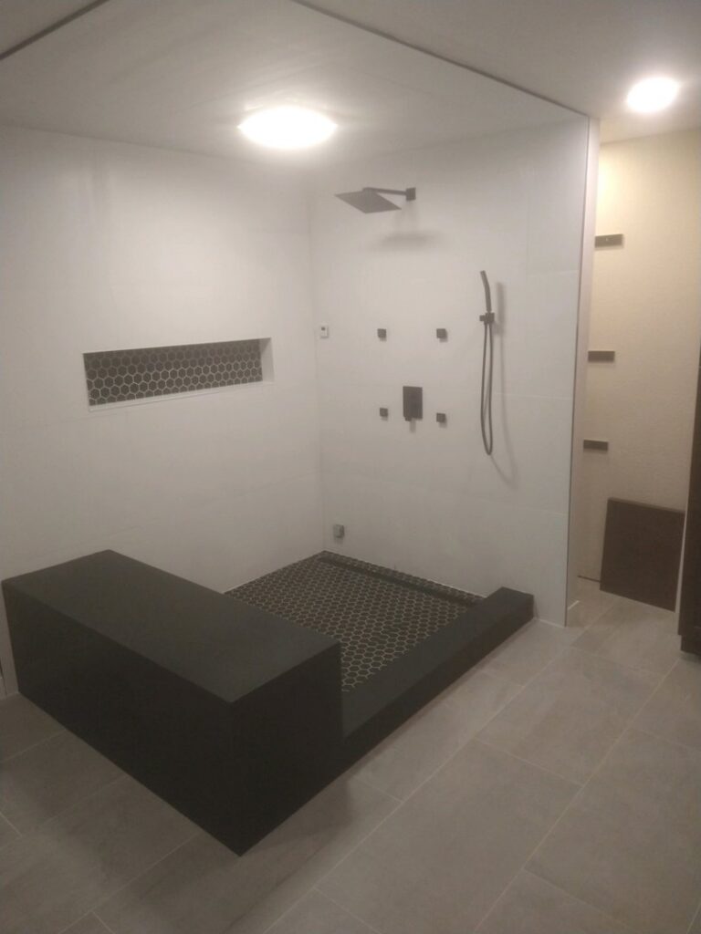 A newly installed modern walk-in shower with a built-in bench and hexagonal tile floor by Mr. Affordable LLC in Denver, CO.