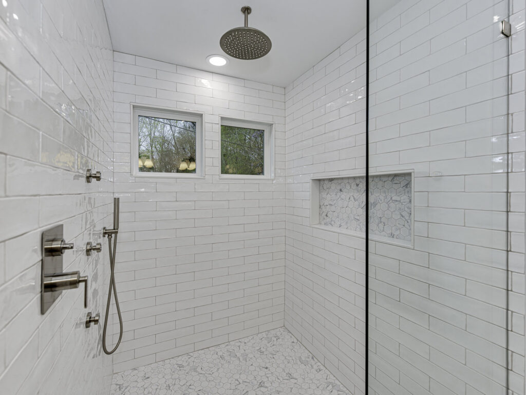 A newly installed walk-in shower with white subway tiles and a pebble floor, a service provided by Boyd's Custom Building in Charlotte, NC.