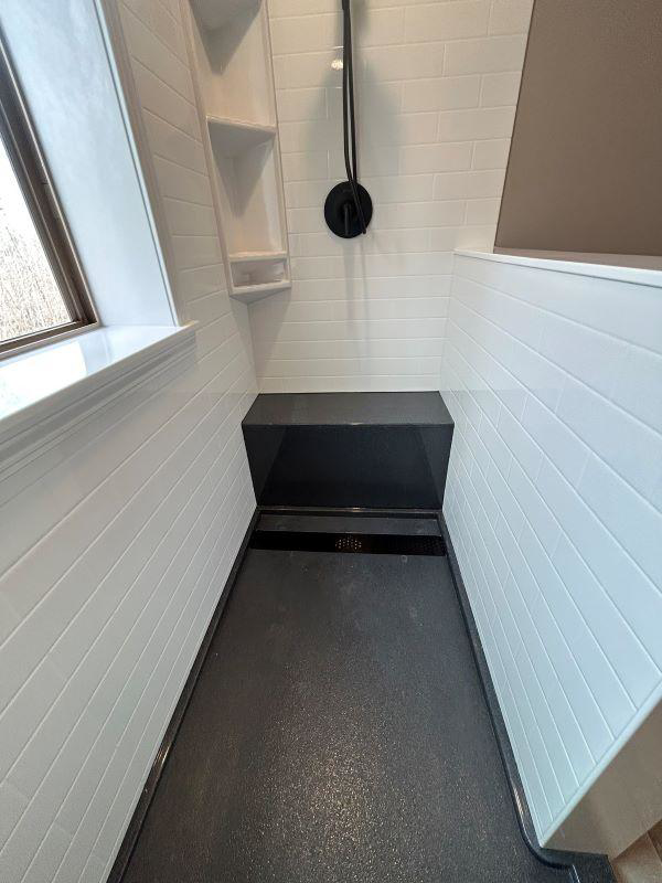 A newly installed walk-in shower with white tiled walls and a black shower pan by VanVleet Construction in Brooklyn Park, MN.