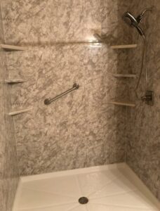 A newly installed walk-in shower with textured wall panels, a grab bar, and built-in shelves by McCollister Contracting LLC in New Castle, DE.