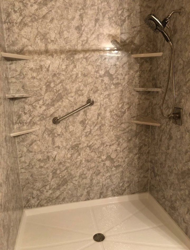 A newly installed walk-in shower with textured wall panels, a grab bar, and built-in shelves by McCollister Contracting LLC in New Castle, DE.