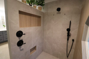 A walk-in shower remodel featuring light grey tiles, black fixtures, and built-in niches by The Bath Shop in Raleigh, NC.