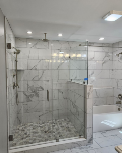 A modern walk-in shower remodel with hexagonal floor tiles and glass enclosure by Total Improvements LLC in San Antonio, TX.