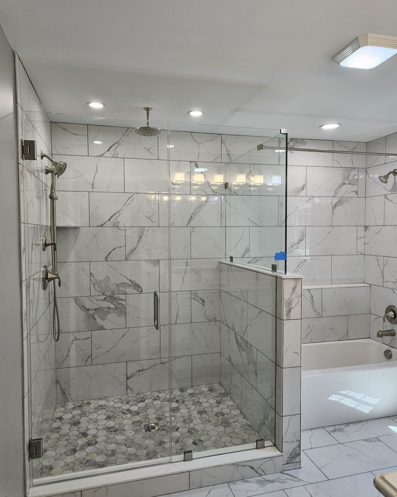 A modern walk-in shower remodel with hexagonal floor tiles and glass enclosure by Total Improvements LLC in San Antonio, TX.
