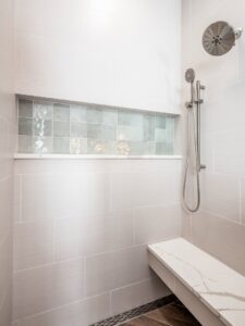 A newly renovated walk-in shower with light gray tiles, a decorative niche, and a built-in bench by Desert Remodel in Scottsdale, AZ.