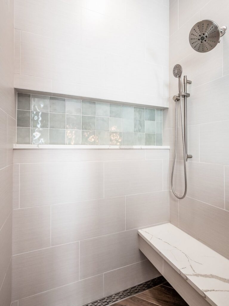 A newly renovated walk-in shower with light gray tiles, a decorative niche, and a built-in bench by Desert Remodel in Scottsdale, AZ.