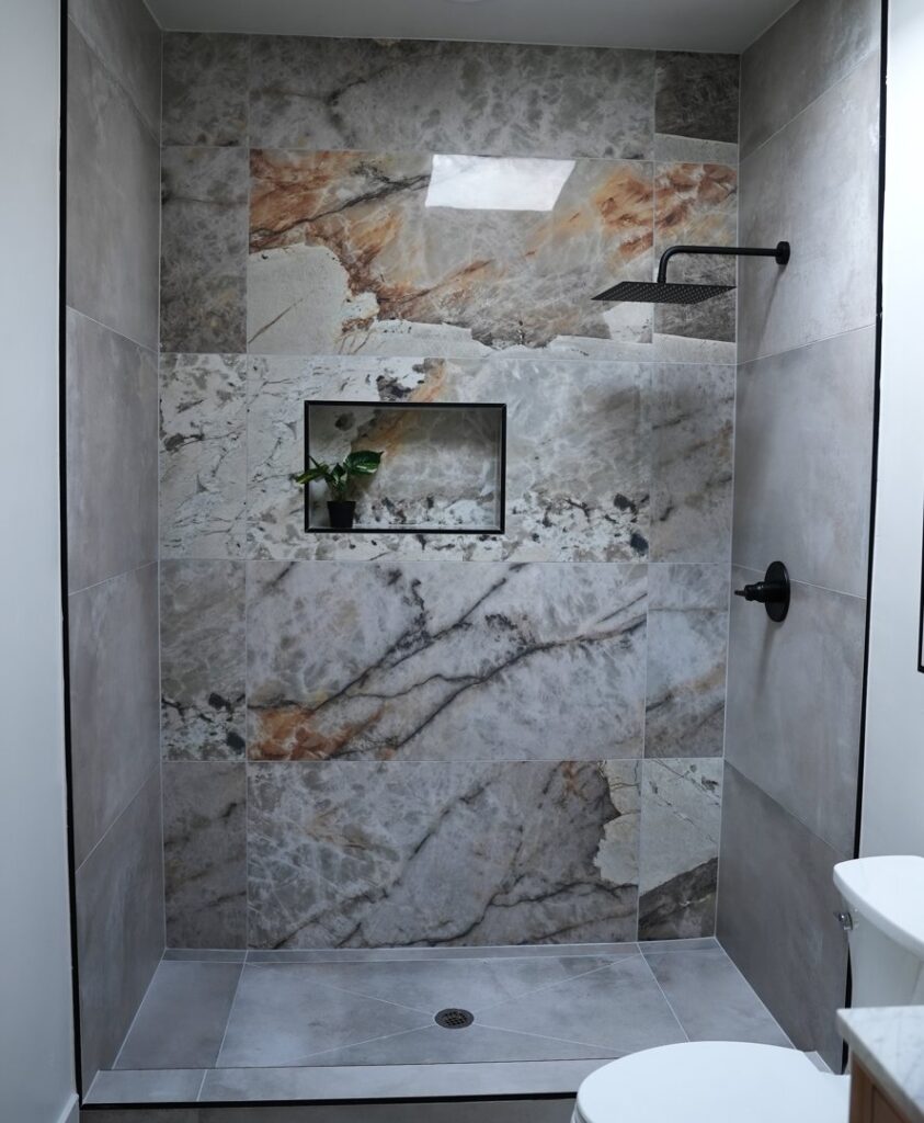 A newly installed walk-in shower with unique marble-look tiles and a modern black shower head by American Wolf Construction in Mesa, AZ